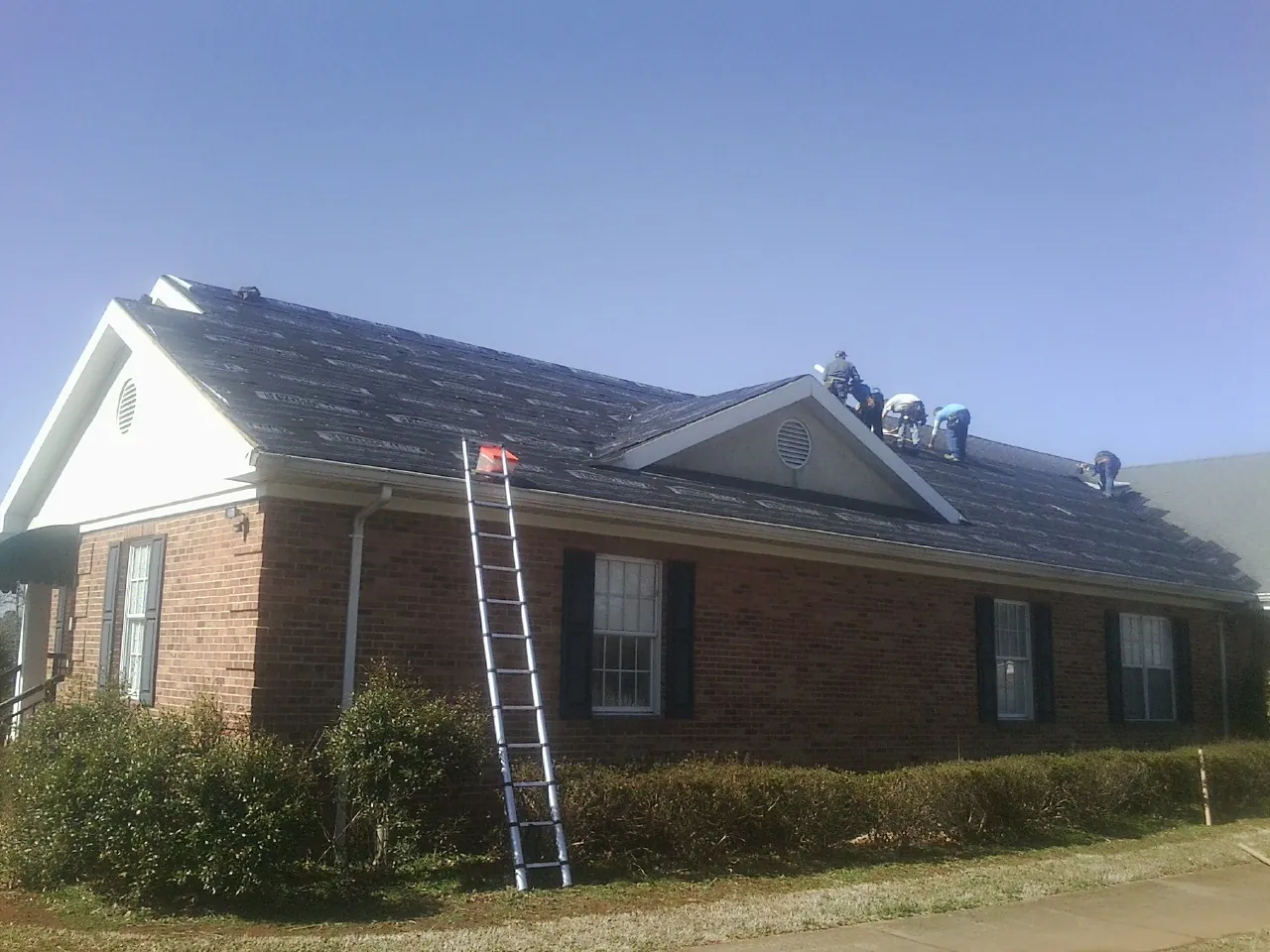 Crew tearing shingles off a brick ranch roof with a ladder set — Metal Roof Repair work by our crew in Porter
