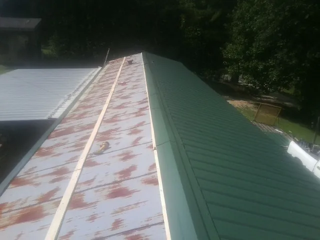 Old rusted panels beside newly installed green metal roofing — Wind Damage Roof Repair by Roofing Brothers in Porter