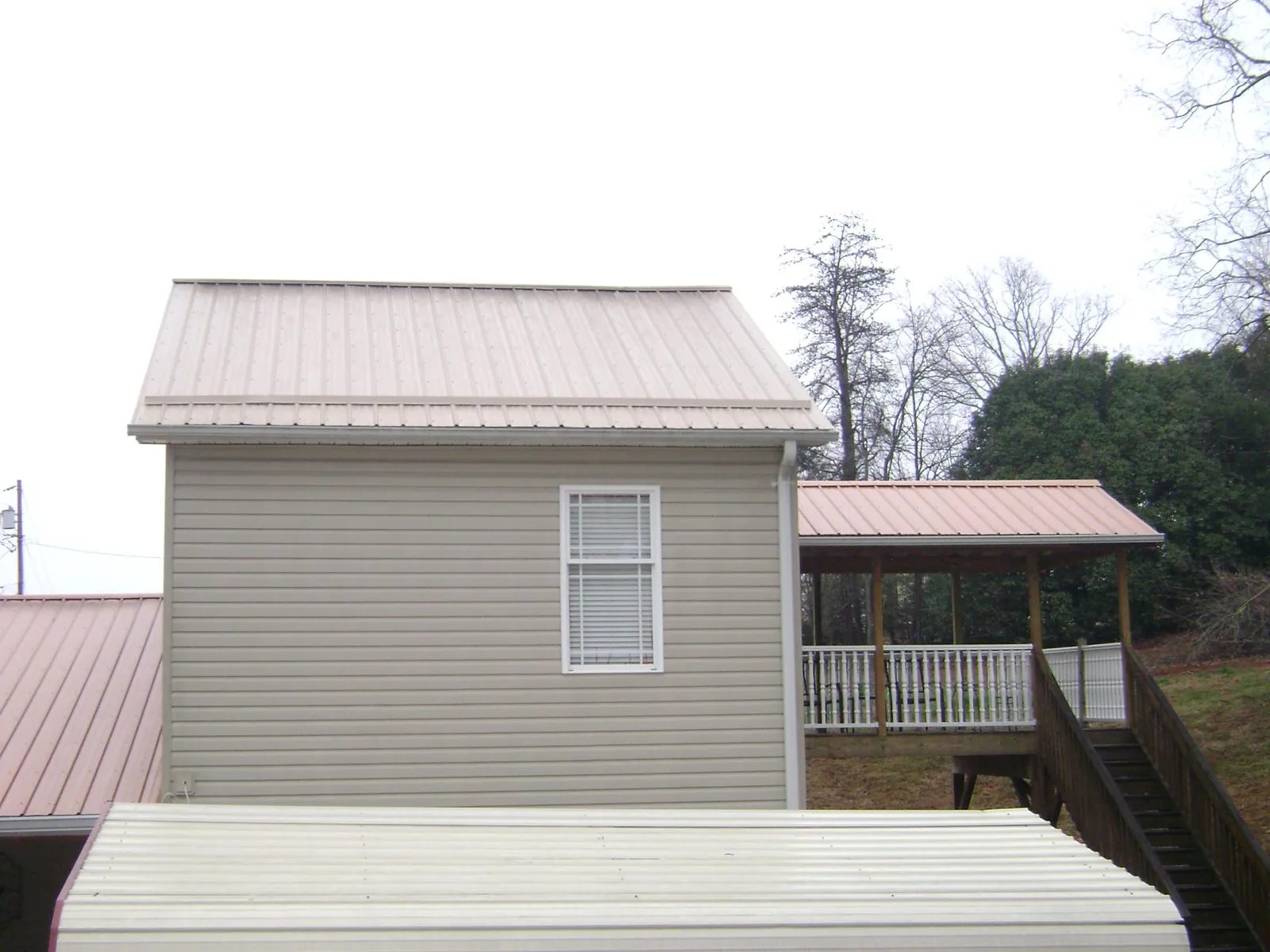 Tan metal roofs on a two story addition and attached porch, from a Roof Replacement job in Porter